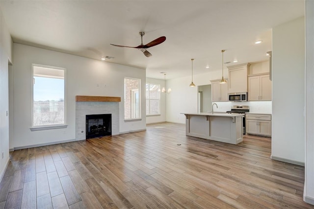 unfurnished living room with sink, light wood-type flooring, ceiling fan with notable chandelier, and a healthy amount of sunlight