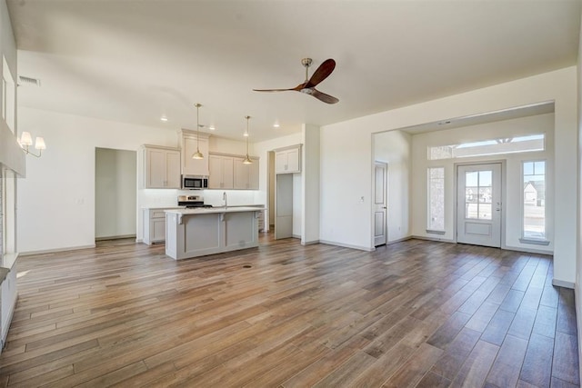 unfurnished living room with sink, light hardwood / wood-style floors, and ceiling fan with notable chandelier