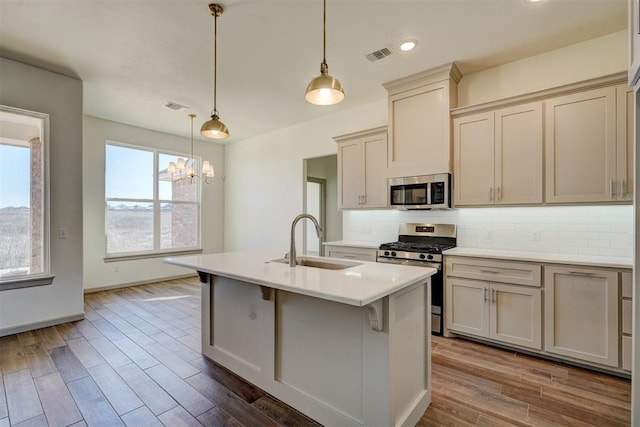 kitchen featuring hanging light fixtures, appliances with stainless steel finishes, sink, hardwood / wood-style floors, and a center island with sink