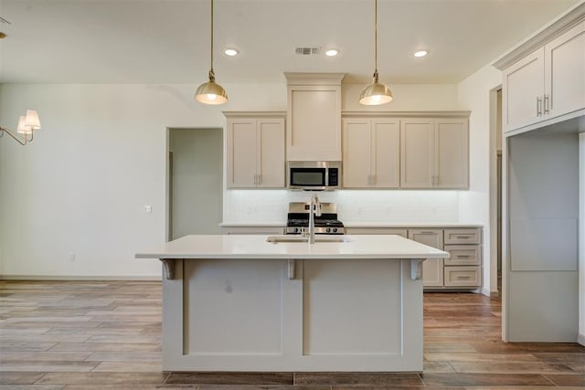 kitchen with light wood-type flooring, hanging light fixtures, a kitchen island with sink, and stove