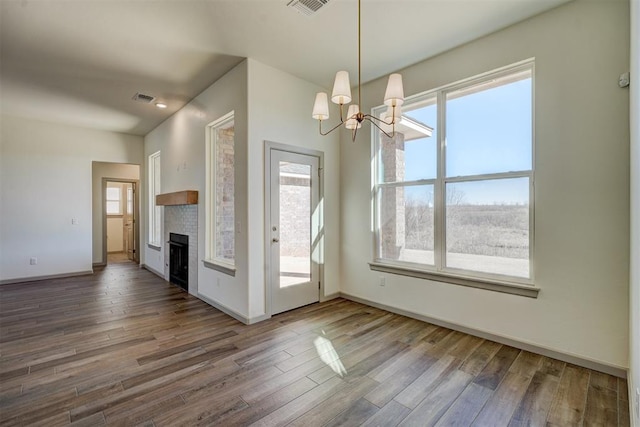 unfurnished dining area featuring a chandelier, a wealth of natural light, a fireplace, and dark hardwood / wood-style flooring