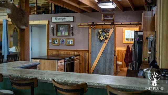 kitchen with black refrigerator, a barn door, beamed ceiling, and wood walls