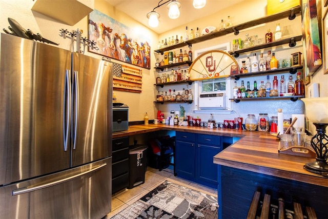 bar featuring butcher block countertops, stainless steel fridge, light tile patterned floors, and blue cabinetry