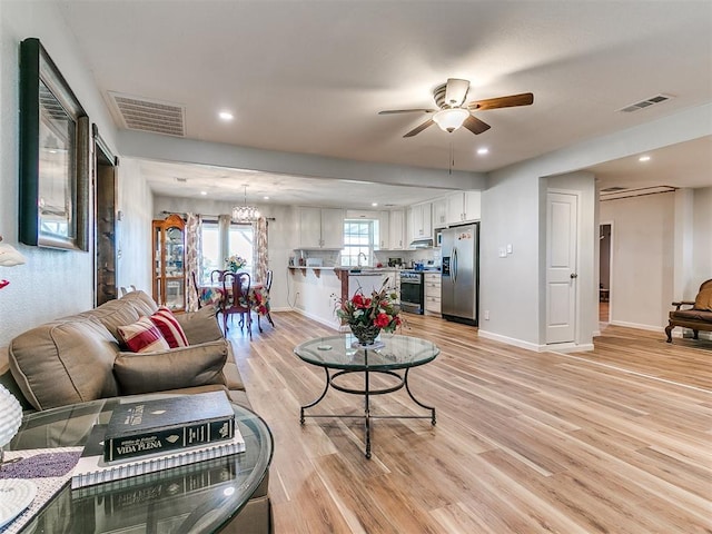 living room with ceiling fan with notable chandelier, light wood-type flooring, and sink