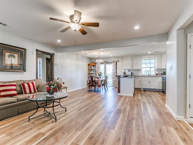 living room with sink, light hardwood / wood-style floors, and ceiling fan with notable chandelier