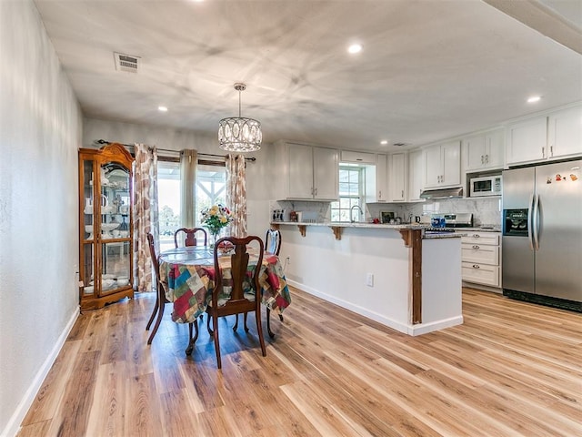 dining space featuring light wood-type flooring, a wealth of natural light, a notable chandelier, and sink