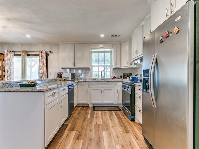 kitchen with white cabinets, light hardwood / wood-style floors, light stone countertops, and appliances with stainless steel finishes