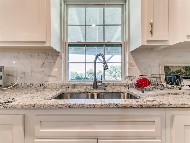 kitchen with backsplash, white cabinets, light stone countertops, and sink