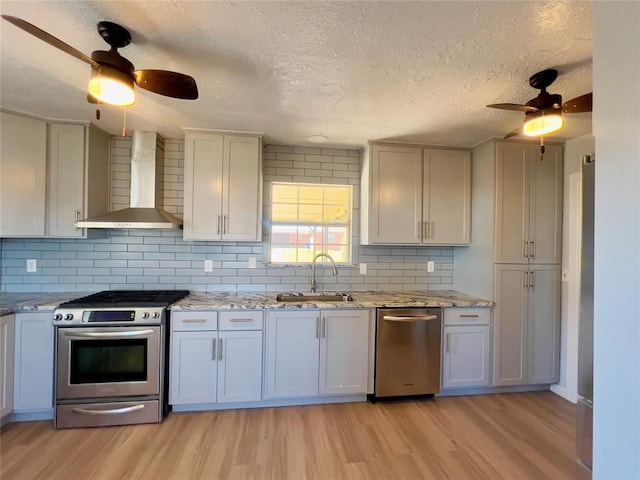 kitchen with white cabinets, wall chimney exhaust hood, light wood-type flooring, and stainless steel appliances