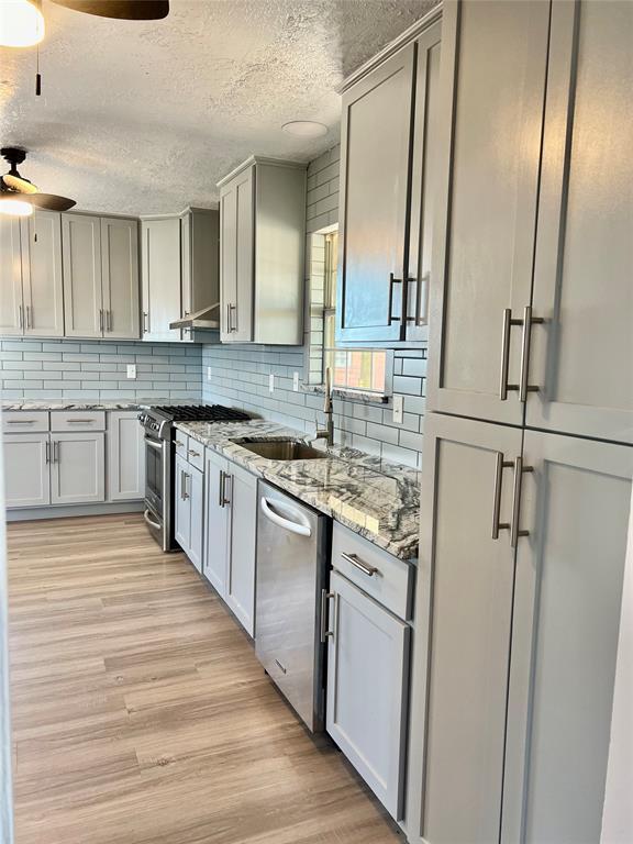 kitchen featuring light wood-type flooring, a textured ceiling, stainless steel appliances, ceiling fan, and sink