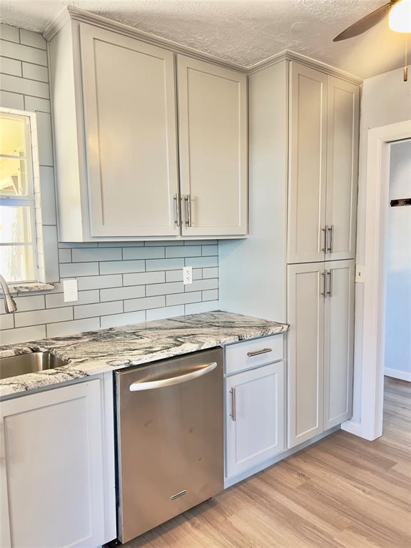 kitchen featuring dishwasher, tasteful backsplash, light stone counters, and light hardwood / wood-style flooring