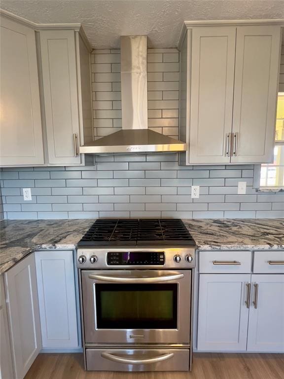 kitchen featuring high end range, white cabinets, wall chimney exhaust hood, and light wood-type flooring