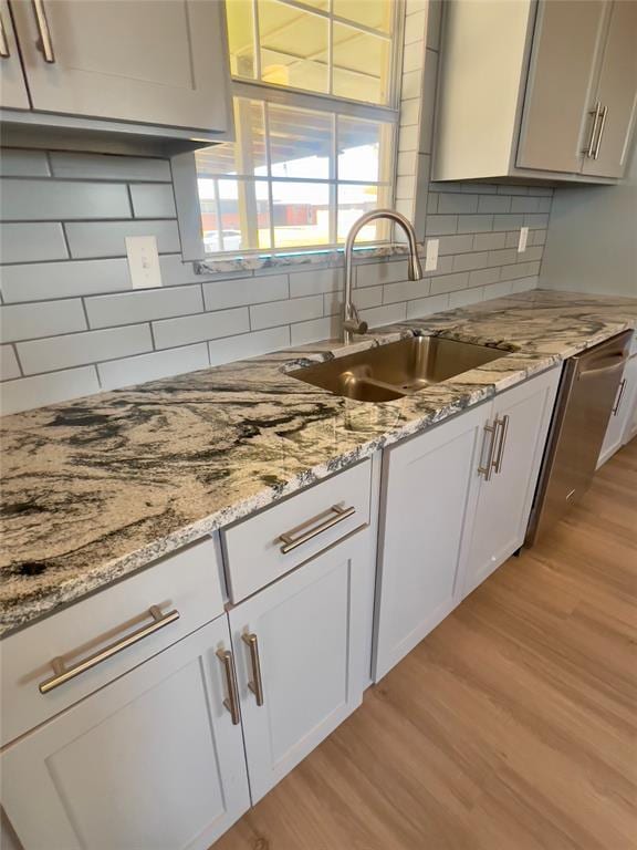 kitchen featuring white cabinets, sink, light wood-type flooring, tasteful backsplash, and light stone counters