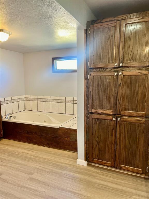 bathroom featuring hardwood / wood-style floors, a textured ceiling, and tiled tub