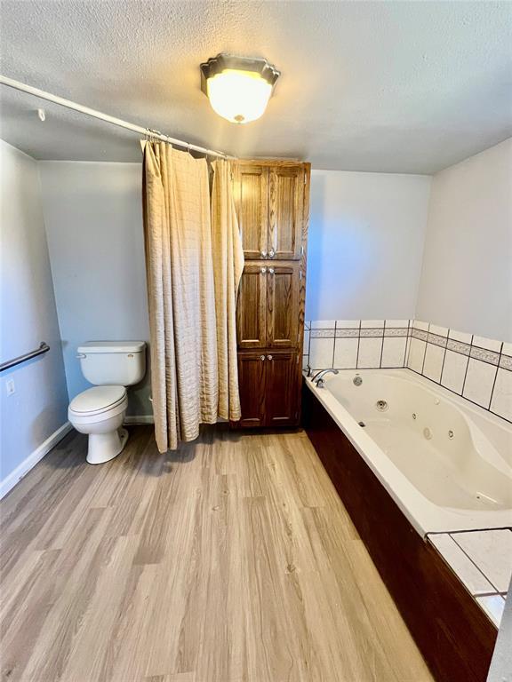 bathroom with a bathing tub, toilet, a textured ceiling, and hardwood / wood-style flooring