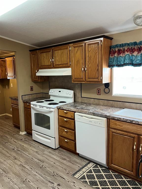 kitchen with sink, ornamental molding, white appliances, and light wood-type flooring