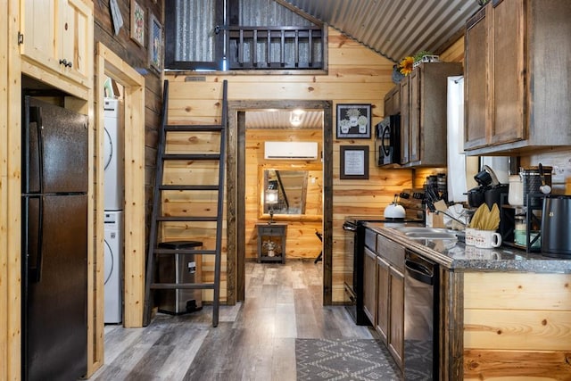 kitchen with black appliances, stacked washer / drying machine, dark hardwood / wood-style floors, and wooden walls