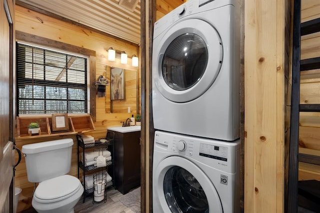 laundry area featuring wooden walls and stacked washer and clothes dryer