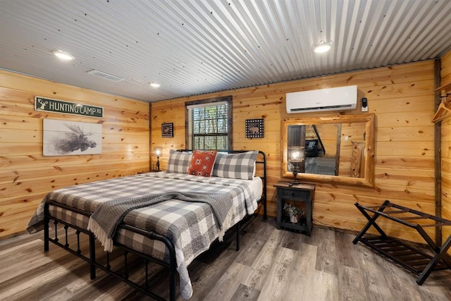 bedroom with hardwood / wood-style flooring, wood walls, and an AC wall unit