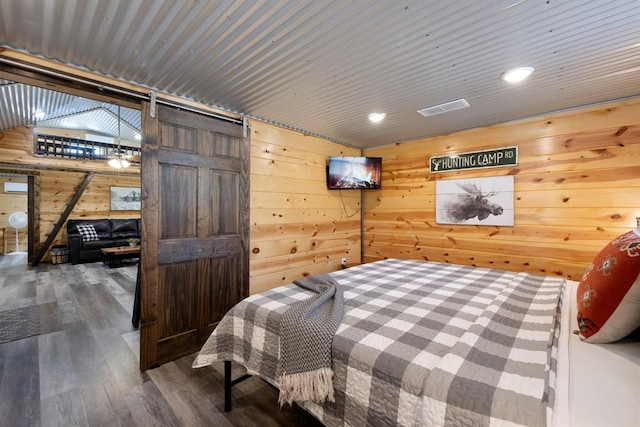 bedroom featuring hardwood / wood-style floors, a barn door, lofted ceiling, and wood walls