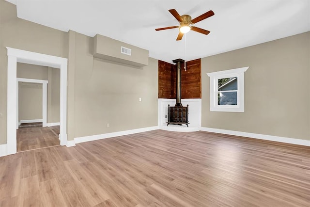 unfurnished living room with a wood stove, ceiling fan, and light wood-type flooring