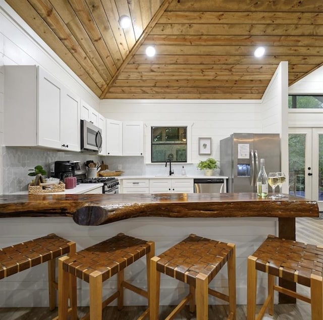 kitchen with wooden ceiling, vaulted ceiling, a kitchen bar, white cabinetry, and stainless steel appliances