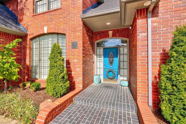 doorway to property featuring brick siding and a shingled roof