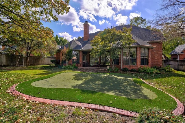 rear view of house with brick siding, a lawn, a chimney, and a fenced backyard