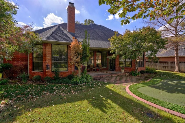 rear view of property with brick siding, fence, a chimney, a yard, and a patio