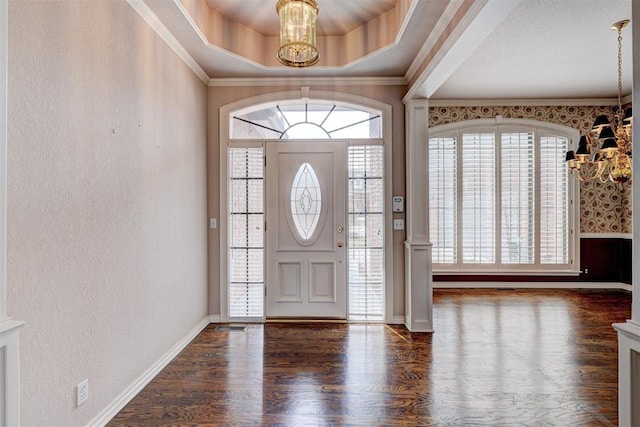 entrance foyer with a raised ceiling, wood finished floors, crown molding, baseboards, and a chandelier