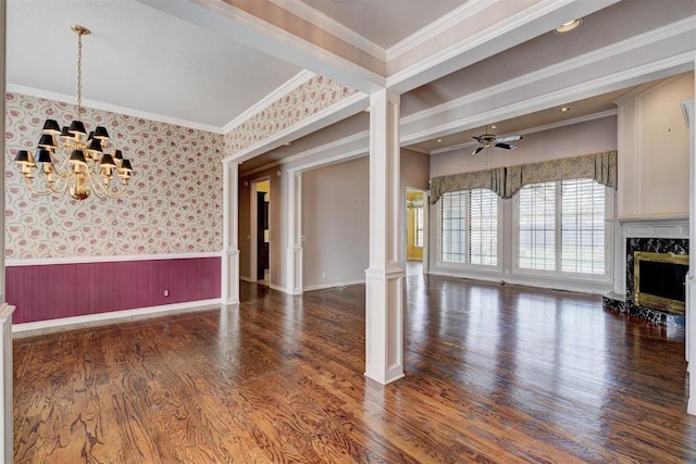 unfurnished living room with a high end fireplace, wallpapered walls, wainscoting, wood finished floors, and ornate columns