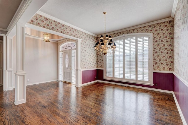 unfurnished room with wallpapered walls, a notable chandelier, wood finished floors, and a wainscoted wall