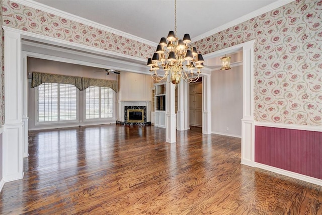 unfurnished living room featuring wood finished floors, a premium fireplace, wallpapered walls, crown molding, and ceiling fan with notable chandelier