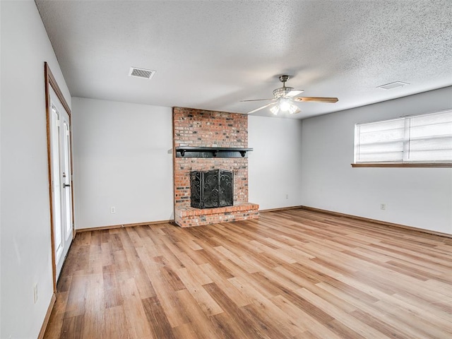 unfurnished living room with a fireplace, a textured ceiling, light wood-type flooring, and ceiling fan