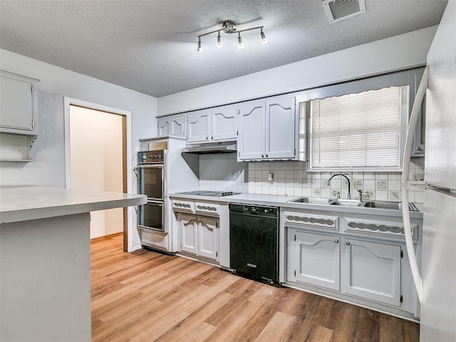 kitchen featuring dishwasher, sink, tasteful backsplash, double oven, and light hardwood / wood-style floors