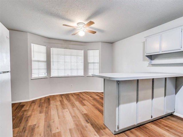 kitchen featuring ceiling fan, kitchen peninsula, a textured ceiling, and light hardwood / wood-style flooring