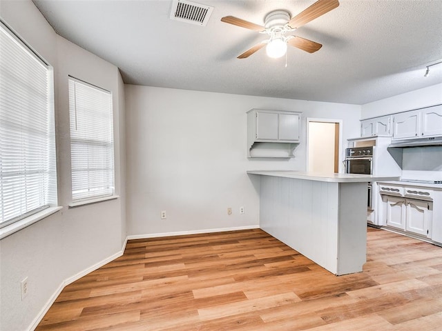 kitchen with kitchen peninsula, white cabinets, oven, and light hardwood / wood-style floors