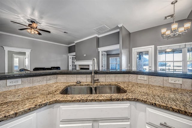 kitchen featuring ornamental molding, ceiling fan with notable chandelier, sink, a tile fireplace, and white cabinets