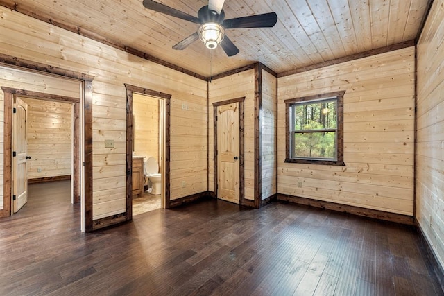 unfurnished bedroom with connected bathroom, wood walls, dark hardwood / wood-style flooring, and ceiling fan