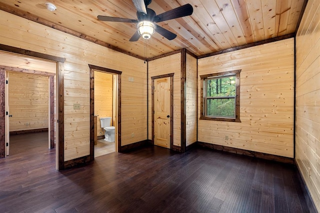 unfurnished bedroom featuring ensuite bath, wooden walls, dark hardwood / wood-style flooring, and ceiling fan