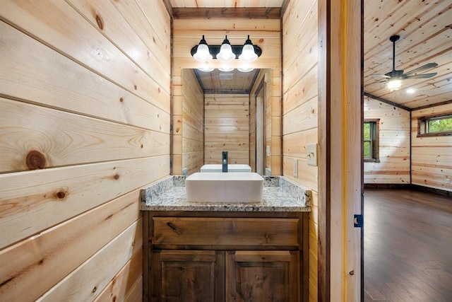 bathroom with hardwood / wood-style floors, vanity, wood walls, vaulted ceiling, and ceiling fan