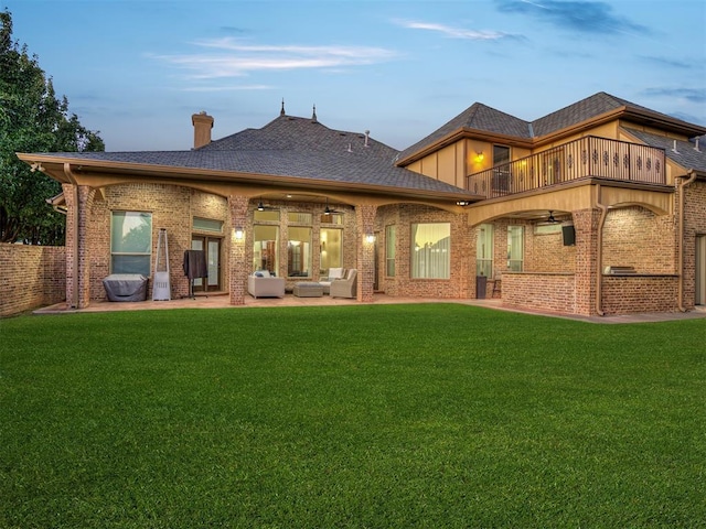 back house at dusk with a yard, an outdoor hangout area, a balcony, and a patio area