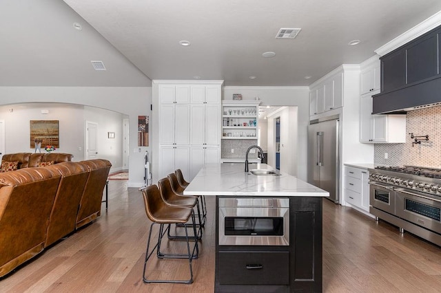 kitchen with sink, light hardwood / wood-style flooring, a kitchen bar, a center island with sink, and high end appliances