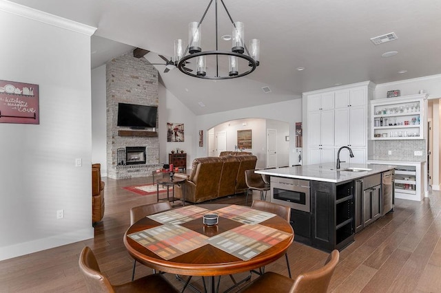 kitchen featuring a center island with sink, a stone fireplace, sink, dark hardwood / wood-style flooring, and white cabinetry