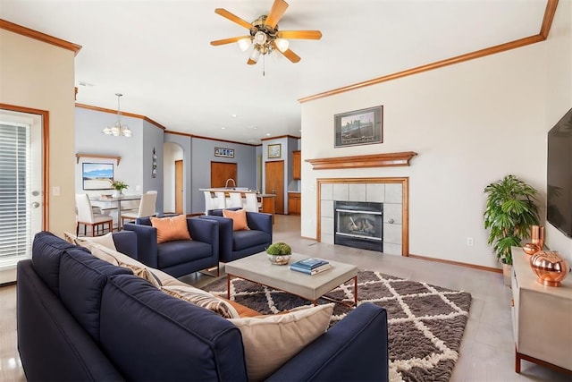 living room with ceiling fan with notable chandelier, light tile patterned flooring, crown molding, and a tile fireplace