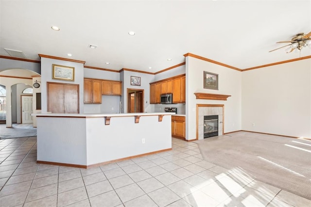 kitchen featuring light carpet, ceiling fan, crown molding, a fireplace, and a kitchen island