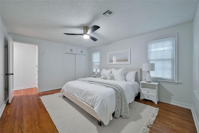 bedroom with ceiling fan, a closet, dark wood-type flooring, and a textured ceiling