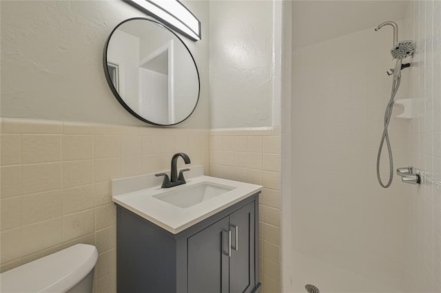 bathroom featuring a tile shower, vanity, toilet, and tile walls