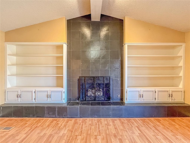 unfurnished living room featuring a textured ceiling, vaulted ceiling with beams, built in features, and dark hardwood / wood-style floors