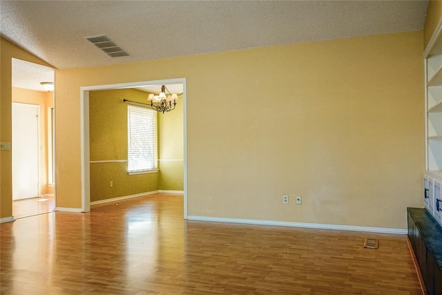 empty room featuring a notable chandelier, lofted ceiling, a textured ceiling, and light hardwood / wood-style flooring